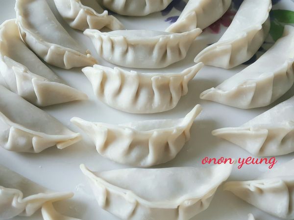 把餡料放在餃子皮中間，邊沿用水黏合，左、右兩端單邊揑出皺摺壓緊。