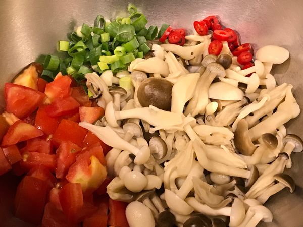 調理盆中加入切丁的番茄、蔥花和辣椒，放入菇類。
