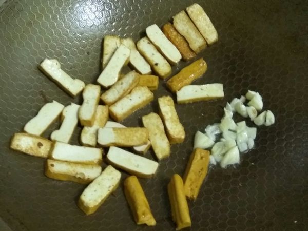 起油鍋，豆干先下鍋煸，上色後翻面，再下蒜頭爆香