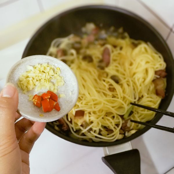 放入煮好的麵拌炒至收汁，加入剩餘的蒜末及辣椒拌炒。