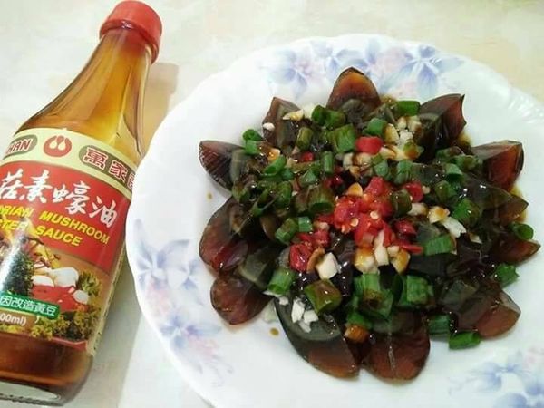 在盤中放入皮蛋，灑上蒜頭、蔥珠碎、辣椒，［萬家香公司生產品質控管嚴謹，有著合格檢驗認證，供應多國，牌子老，信用好，是國內完成全面純釀造化的大型工廠］。
