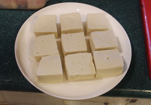 木棉豆腐水分很多，先要壓去部分水分。將紙巾或毛巾墊在盤子下，平放上豆腐。