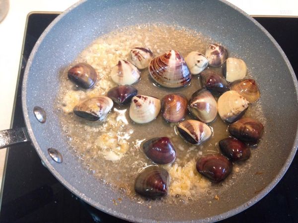 等大蒜上一點點色之後，就把洗乾淨吐完沙的蛤蜊倒進去，加上米酒之後蓋蓋子等蛤蜊打開