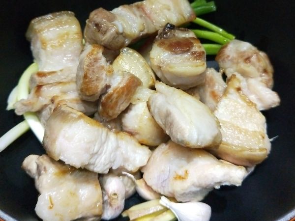 取另一鍋將薑片、蒜頭(不用剝皮）、蔥段放入鍋底，接著放入剛煎的豬肉