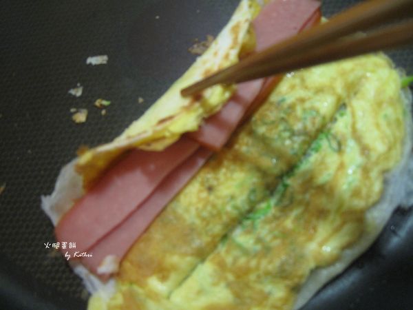 蛋餅翻過來之後就可以鋪上要吃的中間夾層（如：火腿），中間夾層不能太貪心放太厚或太寬，否則會捲不起來。