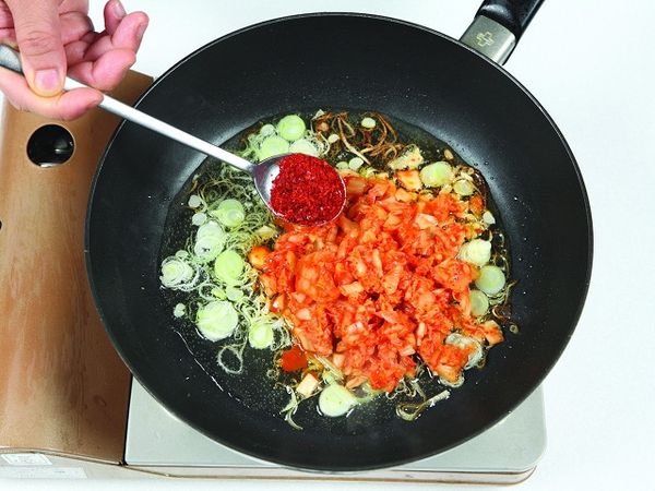 將泡菜和粗辣椒粉放入蔥油裡拌炒。