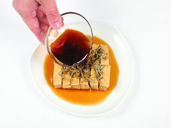 把炸過的鯷魚乾放在豆腐上，並淋下調味醬。