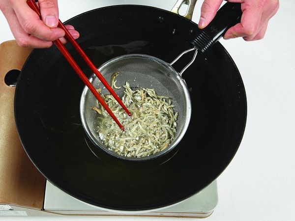 將鯷魚乾放入網篩，放到先前炸過豆腐的油鍋裡酥炸。(也可用蝦米代替鯷魚乾。)