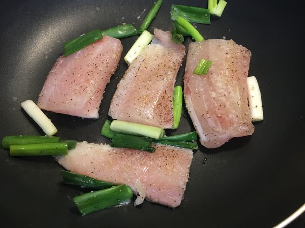 將魚片跟蔥段放人不沾鍋，加鍋蓋煎熟。