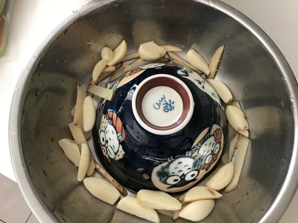 取一個鍋子在鍋中放入一個中碗，並在碗的周遭放入切好的薑絲及蒜頭以及適量的米酒