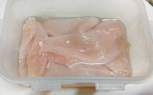 雞胸肉片薄，放入保鮮盒後倒入調勻的鹽水，密封醃漬至少1小時