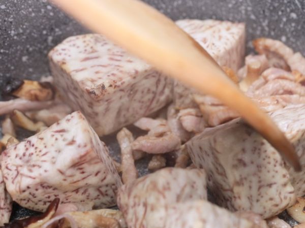 鍋中下油，紅蔥頭、蝦米以小火爆香，放入香菇絲、醃漬過的肉絲、炸過的芋頭，拌炒至肉絲變色。