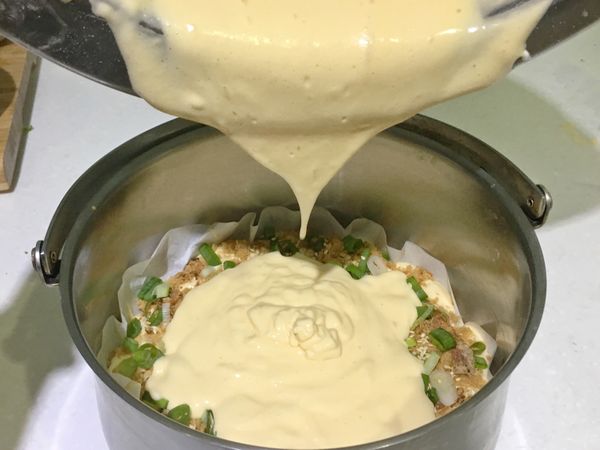 將內提鍋底部鋪上烘焙紙，倒入一半麵糊，均勻撒上一半份量的肉鬆、蔥花、油蔥酥及白芝麻粒；另一半麵糊重覆作法。
