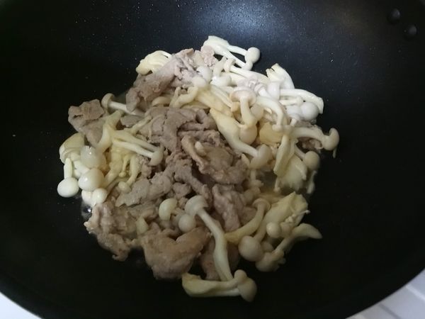 鍋中加入適量的油熱鍋，放入肉片及蒜粒拌炒，炒至肉片變白後再加入雪白菇，雪白菇會漸漸出水變軟