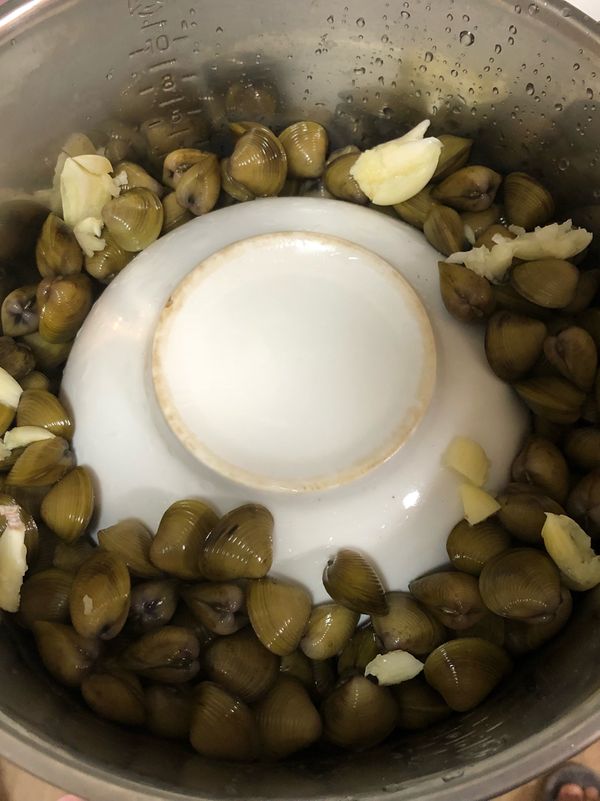 取一鍋子 中間倒放一個碗公 把蜆跟拍過的蒜頭倒下去 電鍋外放一杯水