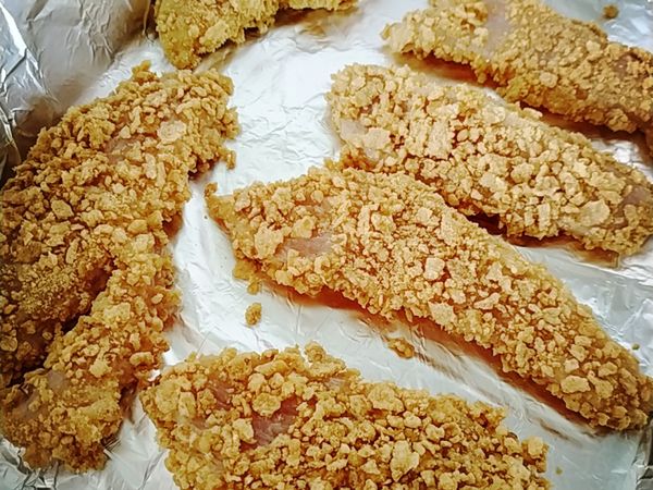 將準備好的雞胸肉均勻裹上碎麥片放入烤盤。