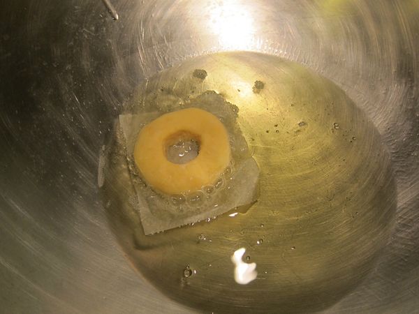 熱油鍋，雙手抓著上面有塑形好的麵糰的烘培紙，（因有烘培紙的關係，雙手不會用力拉扯麵糰，所以不易變形）放進中火中油炸，待烘培紙沾滿油，則可用筷子輕易取出炸鍋，將甜甜圈炸至雙面呈金黃色即可起鍋