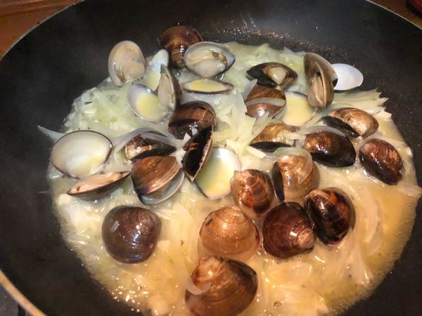 在平底鍋裡, 炒香蒜末跟洋蔥, 再把蛤蠣放入拌炒,倒入白酒。