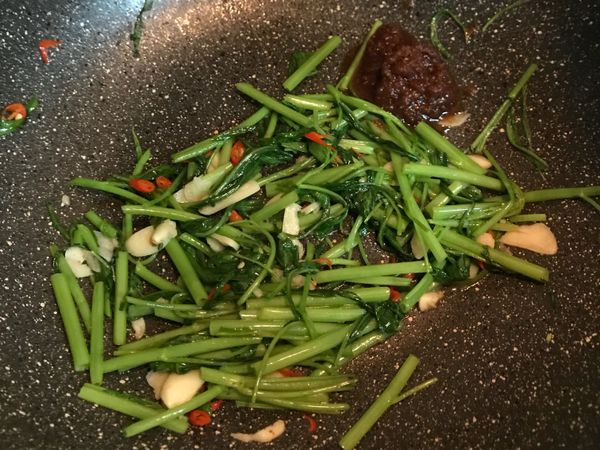 先將空心菜菜梗下鍋並倒入一些水拌炒後，再接著放入菜葉和沙茶醬入炒
