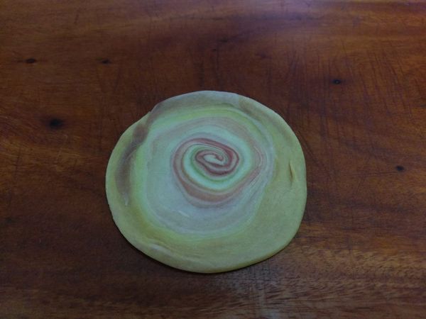 將麵糰對切，切面朝上，用手掌略壓開，再用擀麵棍擀開，擀開面在上，包覆內餡