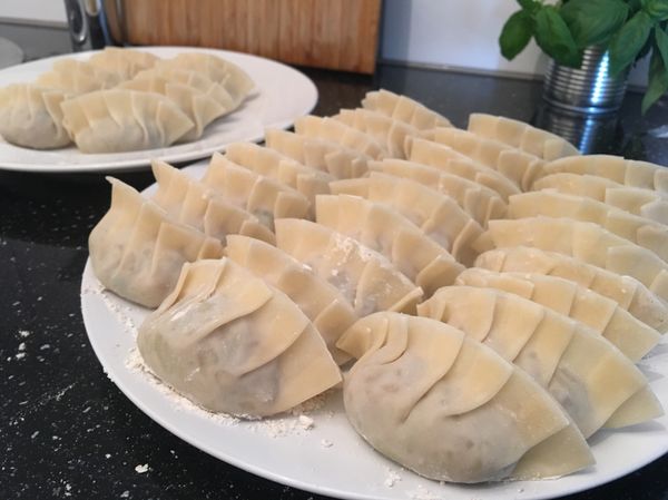 將適量餡料放至餃子皮中，餃子皮邊抹一點水，再將餃子皮對折並折成喜歡的花樣，將折好的餃子放在灑上麵粉的盤子上避免沾黏