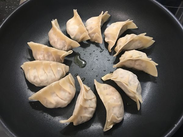 將平底鍋熱鍋，倒入適量油，油熱後將餃子放入鍋中，用中火將餃子底煎至微金黃