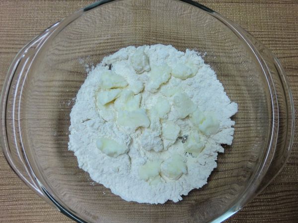 加入切成塊狀的非氫化酥油，輕輕翻拌使油脂表面沾上麵粉。如用無鹽奶油製作，先將切成小塊的奶油放入冷凍庫，冷凍 15~20 分鐘再加入麵粉中。