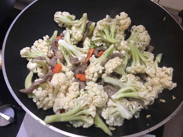 再加入白花椰菜、紅蘿蔔片、鹽、味素（亦可不加）隨後加入半碗水炒勻，即蓋上鍋蓋悶一下。