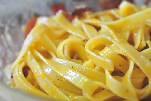 麵起鍋後倒入炒鍋內，加入一匙煮麵水並與培根油拌勻，接著將麵加入步驟 4. 的蛋汁並快速攪勻（若此時培根才剛起鍋，鍋內溫度較高，可以放置十數秒後再與蛋汁混合），最後拌入培根