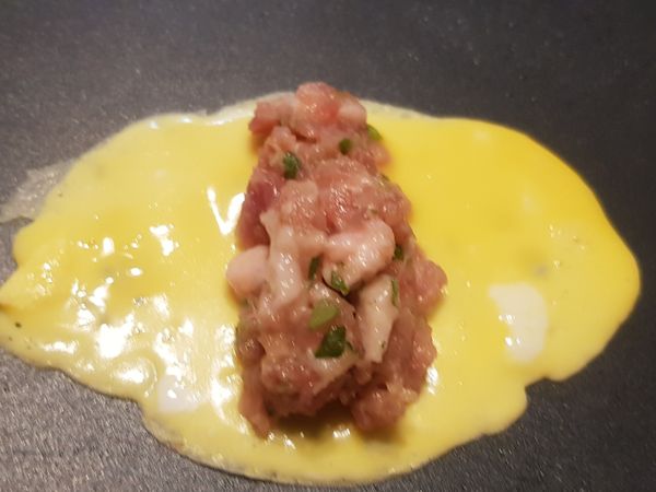 倒入一大匙蛋汁，在蛋汁上放置一份肉餡。