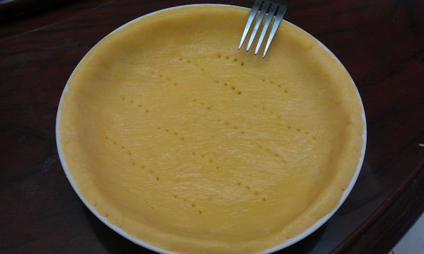 在桌面上舖一層保鮮膜，放上冷藏至稍有硬度的派皮麵糰，再蓋上保鮮膜，稍微壓扁後撖平成約比八吋模型稍大些的圓型。撕開一層保鮮膜，將派皮蓋上模型稍微輕壓與模型貼合後再撕去另一面的保鮮膜，整型好後用叉子在派皮底部均勻戳出小洞，以防止在烤的過程中派皮隆起。放入烤箱中以180度c烤10分鐘。