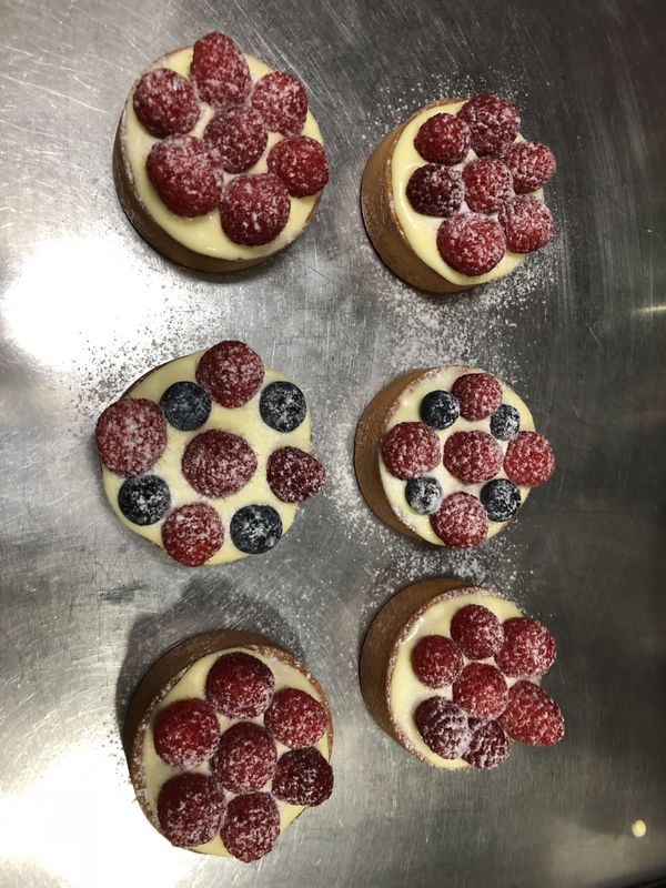 放涼的杏仁甜塔皮擠上卡士達奶油餡，上方再放滿覆盆子及藍莓，最後撒上防潮糖粉點綴