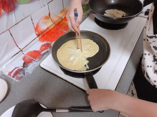 兩支筷子都拉到中間後，開始以中心點小心的旋轉手腕，並依照現場狀況調動鍋柄，使蛋液形成裙擺的感覺。