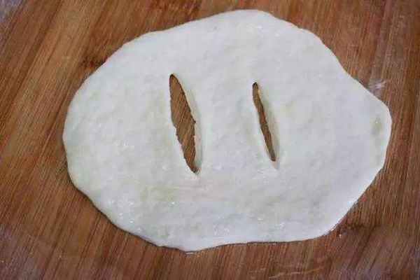 将一个小面团擀成薄饼，用刀在中间划两刀，但不要切断；