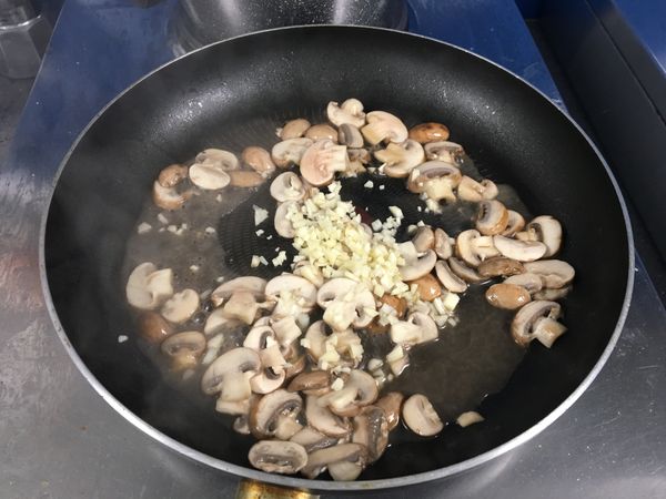 加入橄欖油熱鍋後，切片香菇（蘑菇）下去炒軟（會縮小）後，加入蒜末拌炒出香氣。