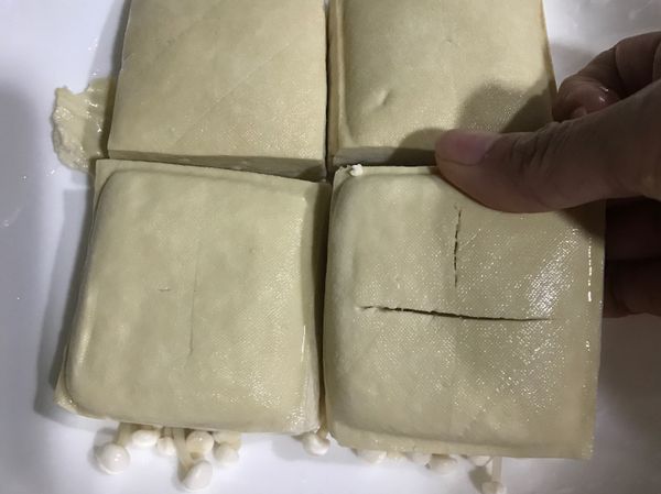 將洗淨的金針菇撥開鋪在最底層，臭豆腐上下兩面都用刀在中心劃十字（以利吸汁入味），鋪在金針菇上。