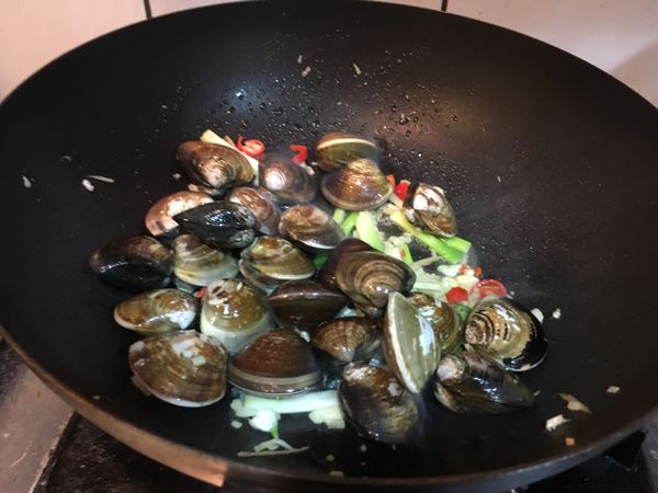 放入蛤蜊稍微翻炒淋入米酒至加蓋煨煮至蛤蜊開。
