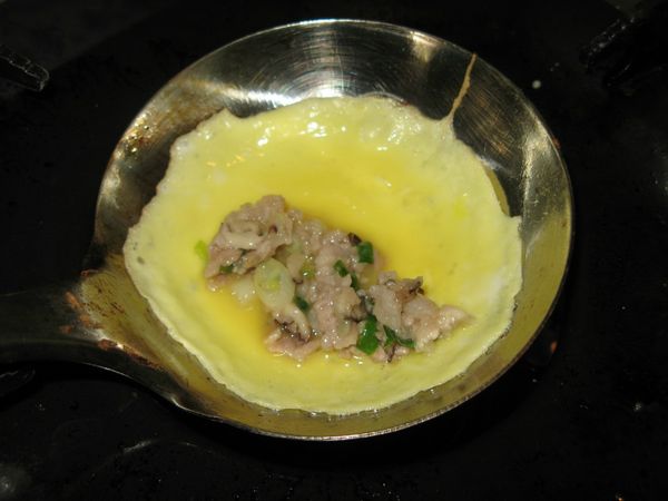 勺少許蛋汁，倒入燒熱的湯杓中央，並且不停轉動湯杓，使蛋液流成圓形煎成圓蛋皮一片。