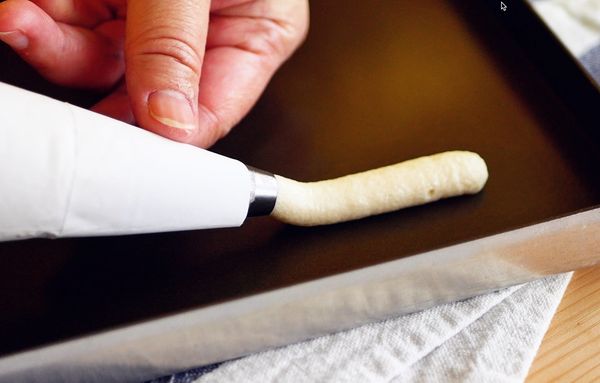 擠花：
先把圓形口徑約 1cm 的花嘴放入擠花袋中，並加入拌好的麵糊，在烤盤上擠出約 7cm 的長條狀，請留意麵糊入烤箱會攤平變寬，麵糊與麵糊之間至少要保留 4cm 以上的距離。