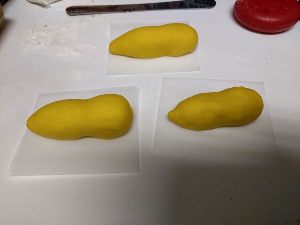 取出靜置後的黃色麵糰整形,分割每個50克的麵糰,滾圓靜置5分鐘後揉成圓長型,再捏出頭和身體