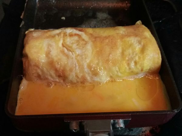 用玉子燒鏟捲起蛋捲2次，推向上方鍋邊，再倒入剩餘蛋液，撒上剩下的乳酪絲。稍微凝固，再用鏟子完全捲起。