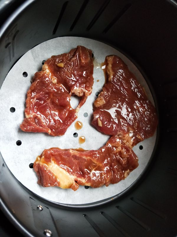 氣炸鍋內鍋放入烘培紙，擺入醃好的肉