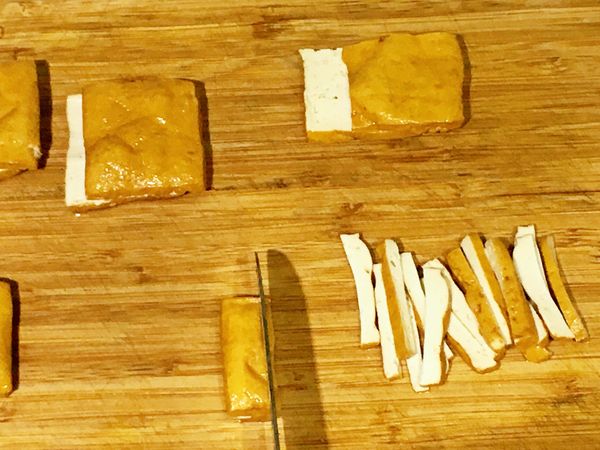 將豆干由橫面剖半，再切成絲狀。