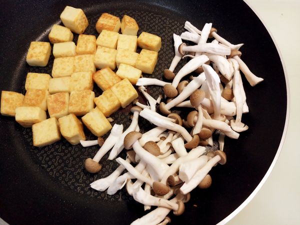 將豆腐丁推至鍋邊，放入鴻喜菇拌炒出香氣
