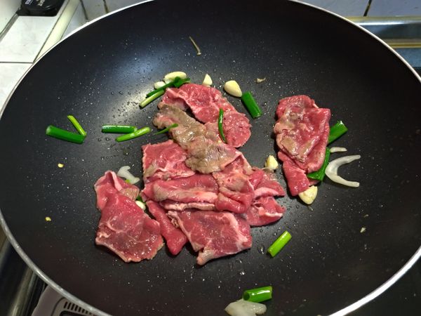另起新鍋爆香蔥段、蒜頭、辣椒，下牛肉片在鍋中一起熱炒。