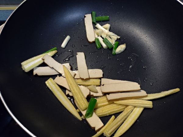 起油鍋先爆香蒜末、蔥段，將玉米筍炒至略軟後，再下切好的豆乾拌炒。