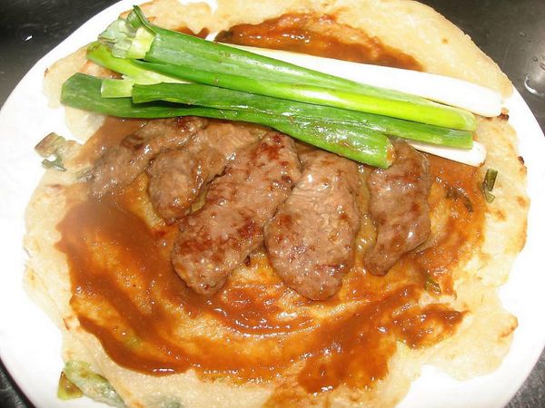 將醬汁沾滿整個蔥油餅，把牛肉片、蔥段放入捲起即可..