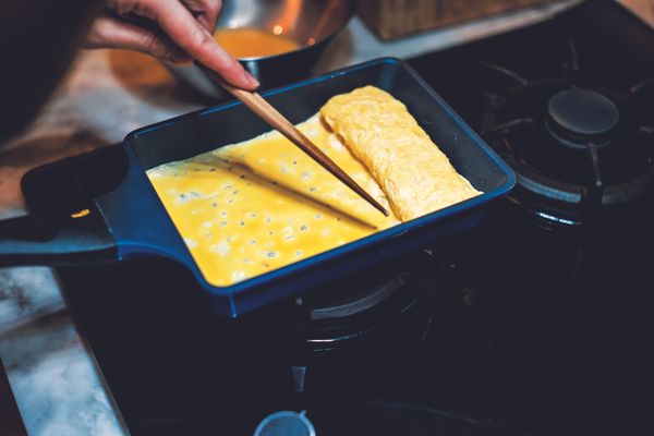 捲到鍋子的一邊後，以剛才擦過鍋底的沾油紙巾，再次抹過鍋底補油。接著，與前一回相同，倒進蛋汁。不同的是，要用筷子把已經捲起來的蛋卷稍微拉起來，讓蛋汁也流進它的下方，才能讓兩者黏著。然後再次把蛋卷順著捲過去，成為更厚實的一捲。