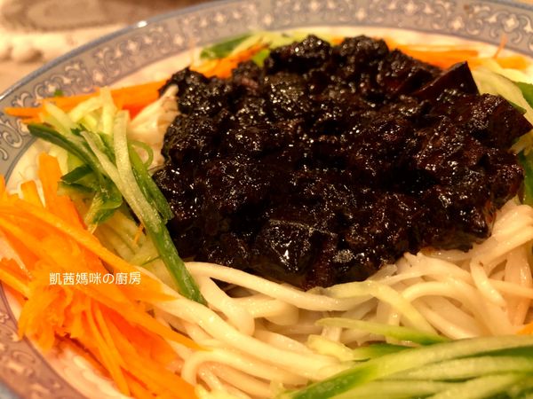 醬料淋在麵條上。小黃瓜、胡蘿蔔刨絲，擺設環繞在炸醬麵。