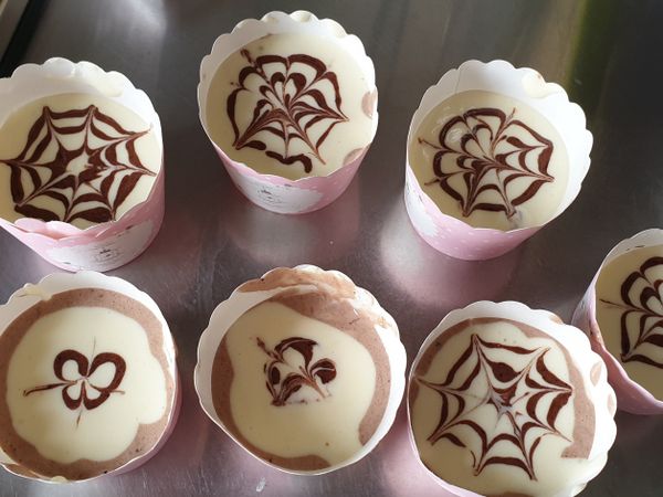 將蛋黃麵糊加入杯中再加入可可麵糊（兩者也可交換喔！），將杯子用力震2下，使其氣泡震出，而剩餘的可可麵糊再加入1-2g可可粉後倒入塑膠袋中，塑膠袋尖角剪一小小洞，於麵糊表面畫同心圓後，再用牙籤往內或往外畫，即完成拉花